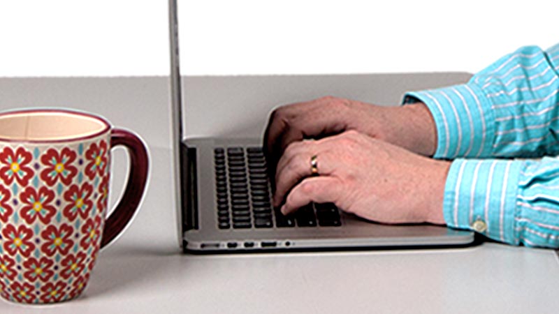 Man's hand typing the keyboard on the laptop. with a coffee mug on the side