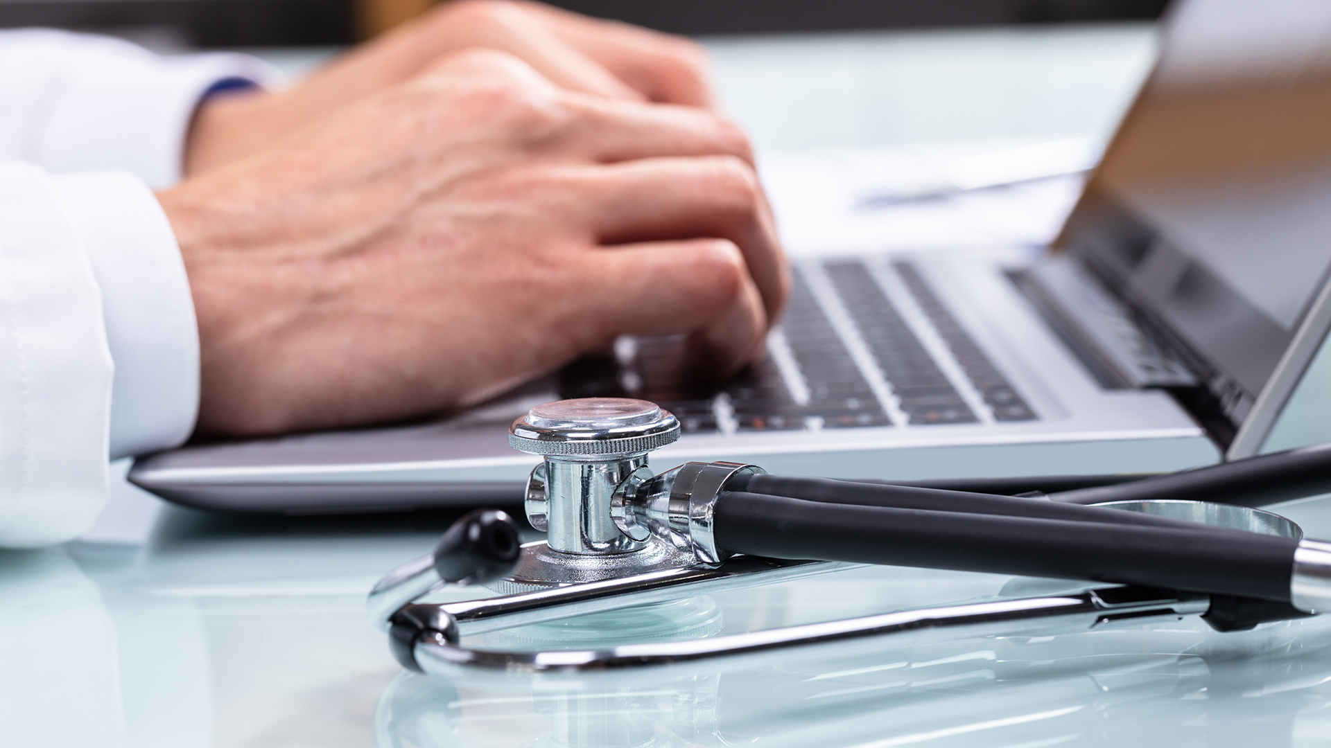 Doctor typing on a laptop with a stethoscope on the side