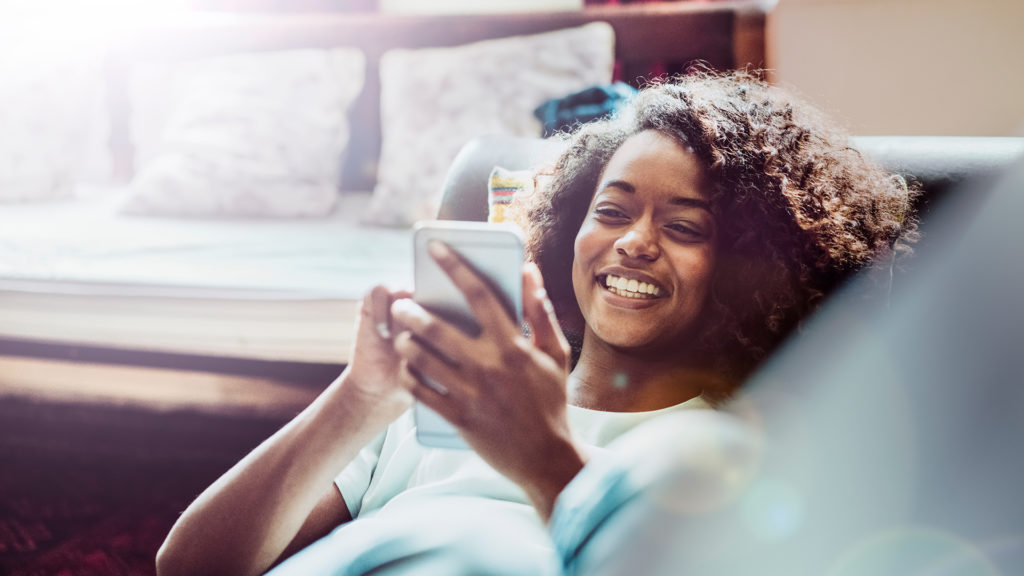 girl on couch smiling looking at mobile phone