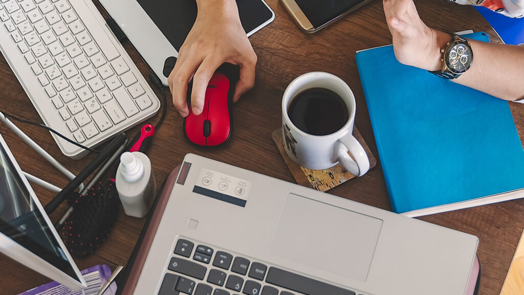 holding mouse while working, work station desk multiple devices, cup of coffee