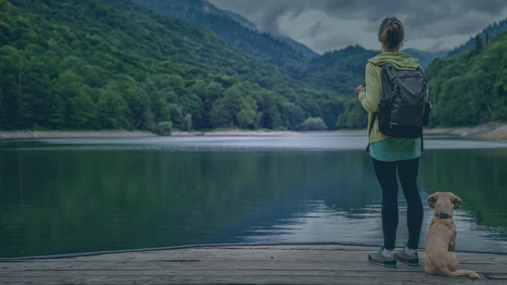 woman backpacking standing by the lake with young dog