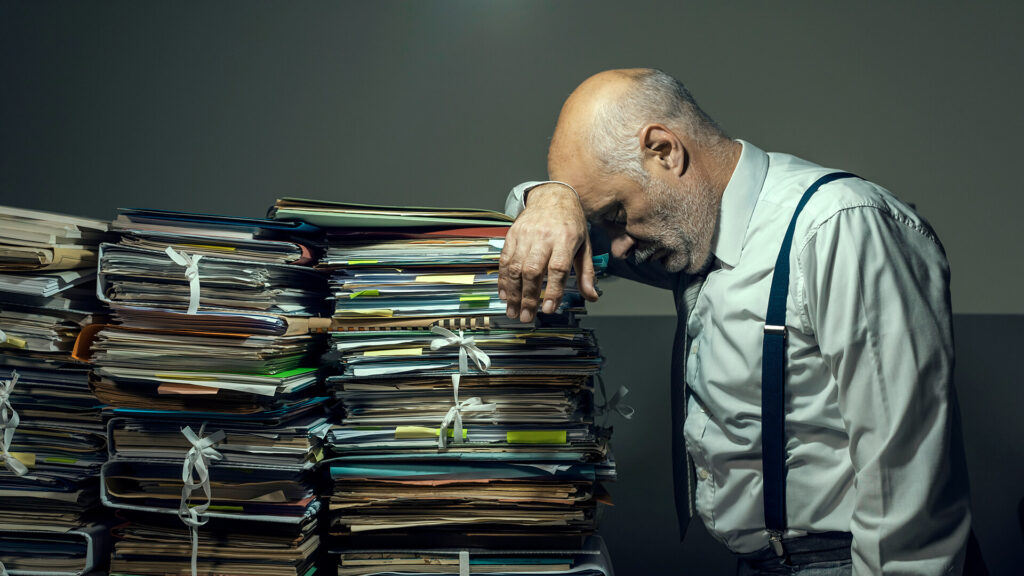 middle aged man tired from work stacked with paperworks